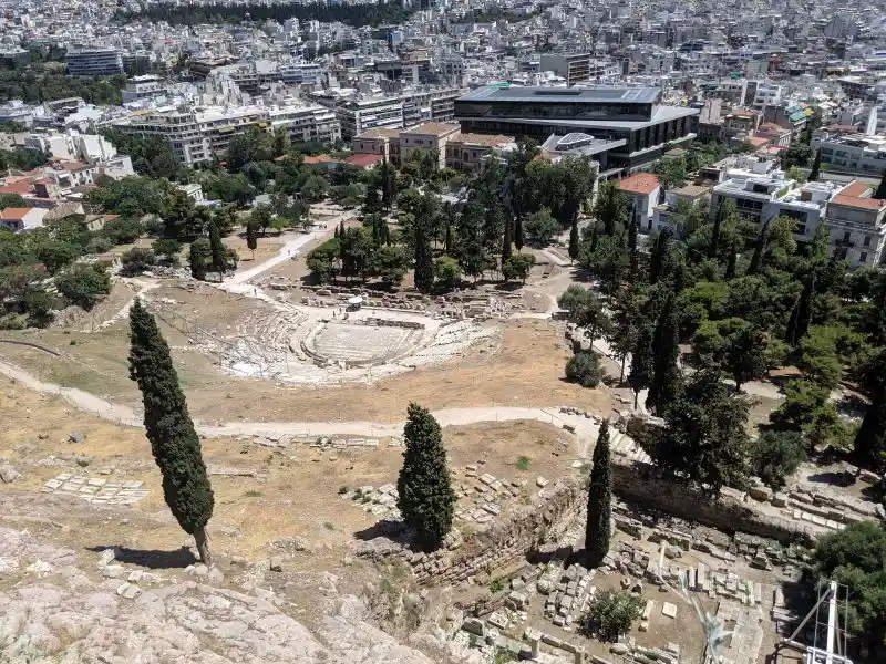 Ancient performance venue on the Acropolis slope with stone seating and cypress backdrop